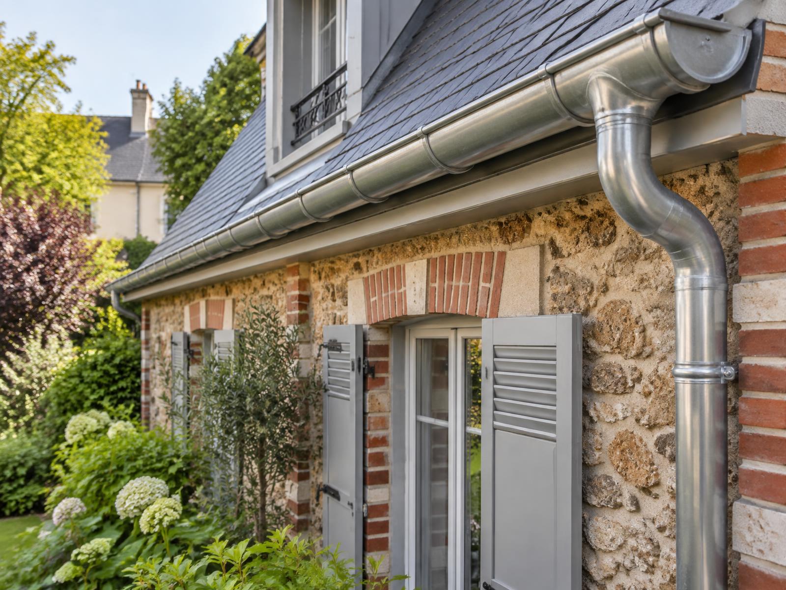 Gouttière en zinc neuve le long d'une toiture en ardoise sur façade meulière